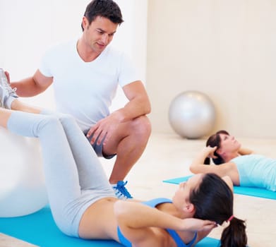 Personal trainer, woman and pilates with ball for workout, training and fitness on floor with support in class. People, coach or instructor helping client with stretching, body exercise and sit up.