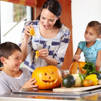 Mother, girl and boy with pumpkins for halloween in the kitchen of their home for holiday celebration. Family, food or tradition and a woman teaching her young children how to carve vegetables.