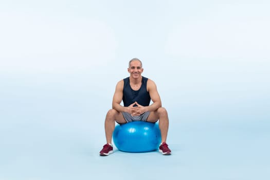 Full body length shot athletic and sporty senior man with fitness exercising ball in sitting posture on isolated background. Healthy active and body care lifestyle after retirement. Clout