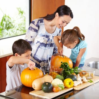 Mother, daughter and son with pumpkins for halloween in the kitchen of their home for holiday celebration. Family, food or tradition and a woman teaching her children how to carve vegetables.