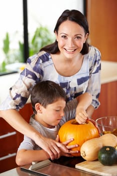 Halloween, pumpkin and a woman in the kitchen with her son for holiday celebration at home. Creative, smile or happy with a mother and boy child carving a face into a vegetable for decoration.