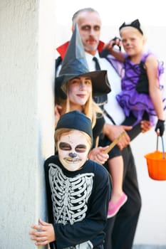 Portrait, halloween and a family in costume for trick or treat tradition or holiday celebration. Mother, father and children at a door in fantasy clothes for dress up on allhallows eve together.