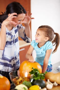 Playful, pumpkin for halloween and a mother with her daughter in the kitchen of their home together for holiday celebration. Smile, happy or funny face with a woman and girl child carving a vegetable.