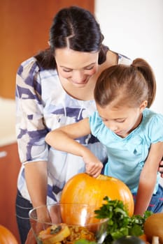 Halloween, pumpkin and a woman in the kitchen with her daughter holiday celebration at home. Creative, smile or happy with a mother and girl child carving a vegetable for decoration or tradition.