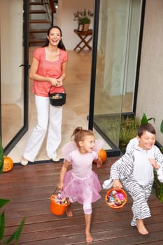 Family home, halloween and children running with candy for fun, adventure or vacation tradition. Happy, love and mother watching excited kids in costume, laugh and playful energy for holiday prank.