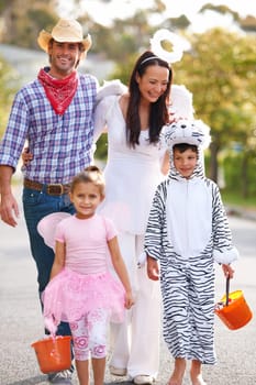 Halloween, celebration and happy family walking in a street with love, smile and excited for vacation tradition. Costume, support and children with parents in a road for neighborhood candy collection.