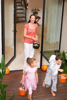 Family house, halloween and children running with candy for fun adventure or vacation tradition. Happy, love and mom watching kids in costume with candy, laugh and energy in costume for holiday prank.