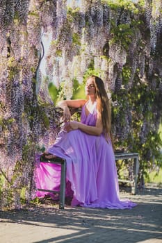 Woman wisteria lilac dress. Thoughtful happy mature woman in purple dress surrounded by chinese wisteria.