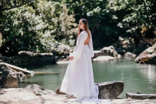 a beautiful woman in a long white dress looks into the distance at a beautiful lake with swans