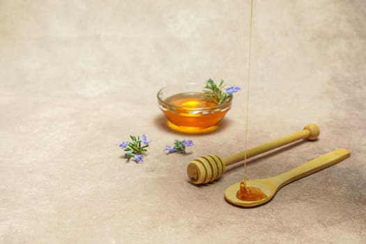 natural rosemary honey dripping on a wooden spoon with rosemary blossom branches and a bowl with honey