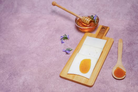 slices of cheese with honey on a wooden board with fresh rosemary blossoms and a glass bowl with rosemary honey