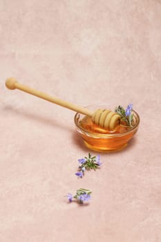 natural honey in a glass bowl with a wooden spoon and fresh rosemary sprigs in bloom