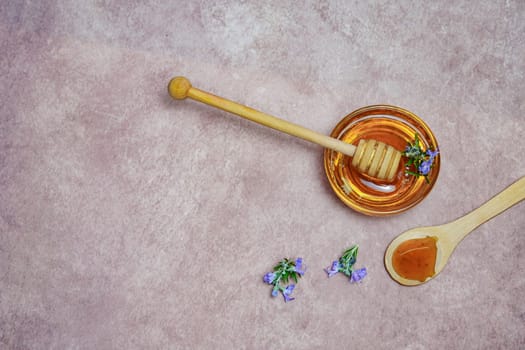 top view of natural rosemary honey in a glass bowl with a wooden spoon and fresh rosemary branches in blossom