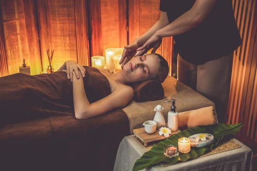 Caucasian woman enjoying relaxing anti-stress head massage and pampering facial beauty skin recreation leisure in warm candle lighting ambient salon spa in luxury resort or hotel. Quiescent