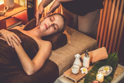 Caucasian woman enjoying relaxing anti-stress head massage and pampering facial beauty skin recreation leisure in warm candle lighting ambient salon spa in luxury resort or hotel. Quiescent