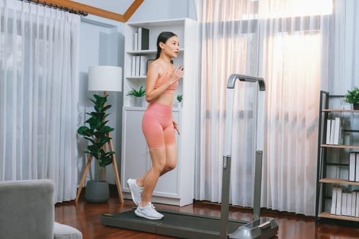 Energetic and strong athletic asian woman running running machine at home. Pursuit of fit physique and commitment to healthy lifestyle with home workout and training. Vigorous