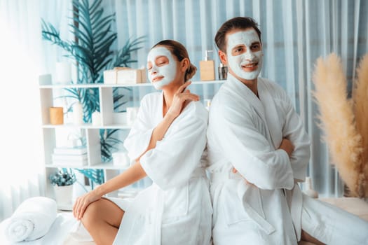 Blissful couple in bathrobe with facial cream mask enjoying serene ambiance of spa salon resort or hotel during holiday. Pampering face spa and skincare treatment with essence relaxation. Quiescent