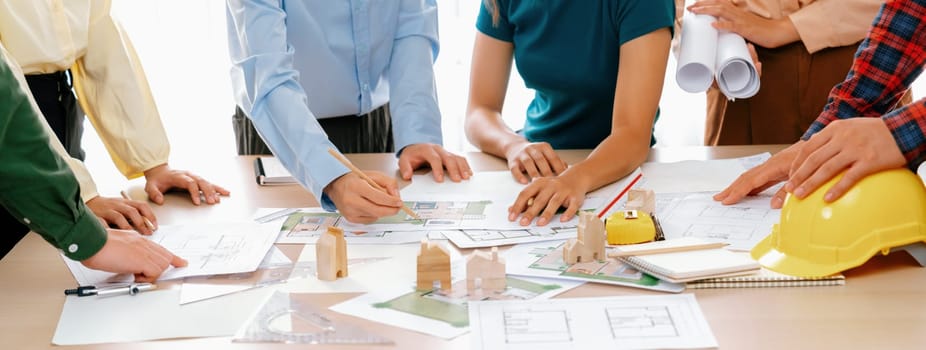 Professional architect engineer team discussion about architectural project on meeting table with wooden block and blueprint scatter around. Design and cooperate concept. Closeup. Delineation.