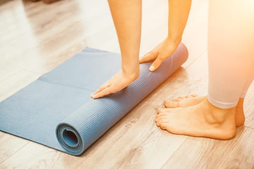 Woman hands rolled up yoga mat on gym floor in yoga fitness training room. Home workout woman close up hands rolling foam yoga gym mat. Woman barefoot home workout sportive healthy lifestyle concept.
