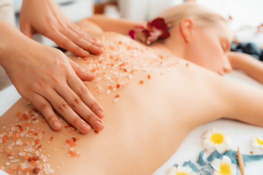 Closeup woman customer having exfoliation treatment in luxury spa salon with warmth candle light ambient. Salt scrub beauty treatment in health spa body scrub. Quiescent