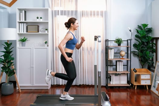 Full length side view of energetic and strong athletic asian woman running running machine at home. Pursuit of fit physique and commitment to healthy lifestyle with home workout and training. Vigorous