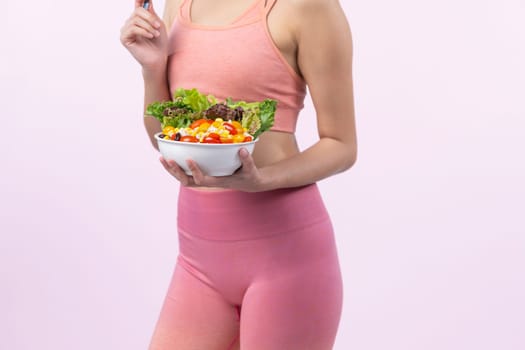 Young sporty Asian woman in sportswear holding salad bowl fill with vibrant of fruit and vegetable. Natural youthful and fit body lifestyle with balance nutrition on isolated background. Vigorous