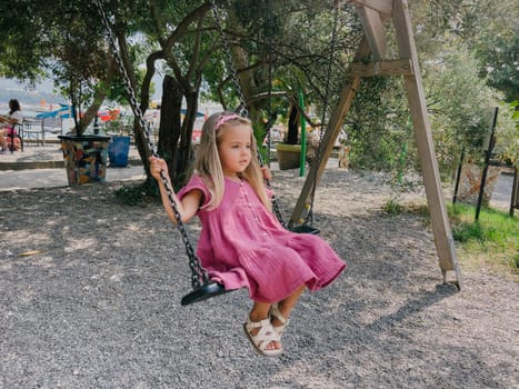 Little girl in a pink dress swings on a chain swing in the park. High quality photo