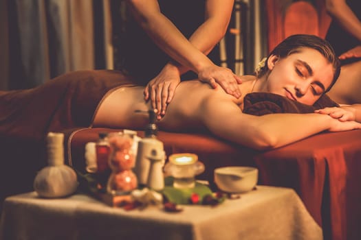 Caucasian couple customer enjoying relaxing anti-stress spa massage and pampering with beauty skin recreation leisure in warm candle lighting ambient salon spa at luxury resort or hotel. Quiescent