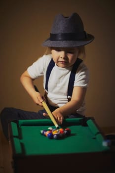 Charming child in retro clothes playing toy billiards.