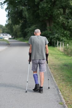 A man with a broken leg is walking down the street, on his left leg he has a special boot for walking, if the leg is in a cast, the man moves with the help of crutches,high quality photo