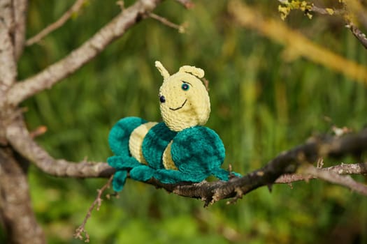 Knitted toy caterpillar on a tree in the garden.