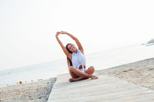 woman with long hair doing yoga on the beach by the sea