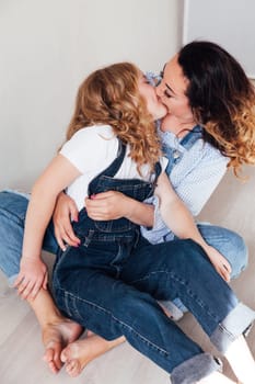 Mom and daughter in jeans sit together cuddling kisses