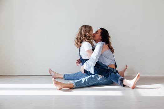 Mom and daughter in jeans sit together cuddling kisses