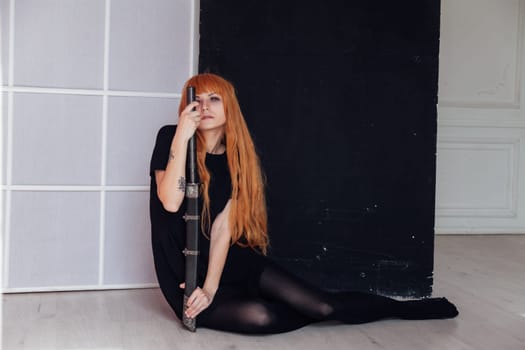 A female cosplayer with red hair sits on the floor holding a Japanese sword
