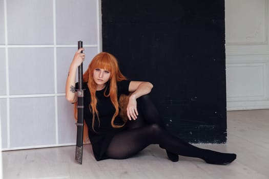 A female cosplayer with red hair sits on the floor holding a Japanese sword