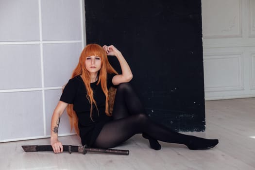 A female cosplayer with red hair sits on the floor holding a Japanese sword