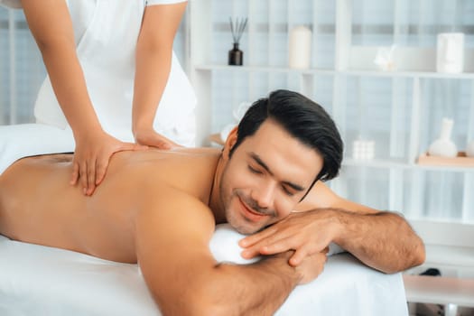 Caucasian man customer enjoying relaxing anti-stress spa massage and pampering with beauty skin recreation leisure in day light ambient salon spa at luxury resort or hotel. Quiescent