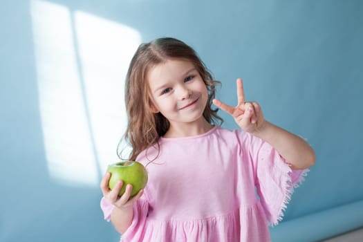 Beautiful little girl with green apple shows two fingers