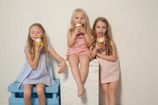 Three fashionable little girls in light dresses eat candy lollipop