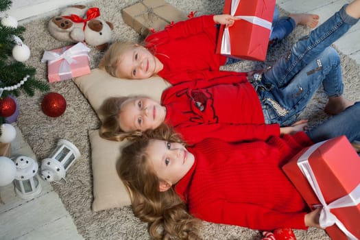 Three little girl girlfriends open Christmas presents to the new year