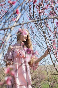 A woman blonde in a pink dress walks through the flowering peach garden