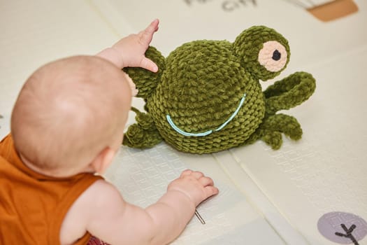baby plays with a knitted toy in the nursery.
