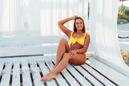 Tanned woman in swimsuit with long hair sits in the shade on the beach