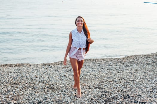 woman with long hair walks on beach by the sea