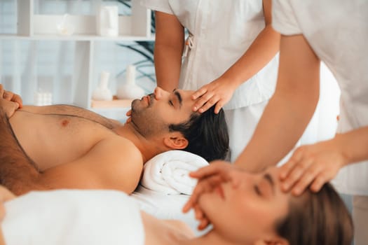 Caucasian couple enjoying relaxing anti-stress head massage and pampering facial beauty skin recreation leisure in dayspa modern light ambient at luxury resort or hotel spa salon. Quiescent