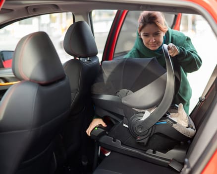 A Caucasian woman puts a child seat with a newborn baby in the car. Quick fastener