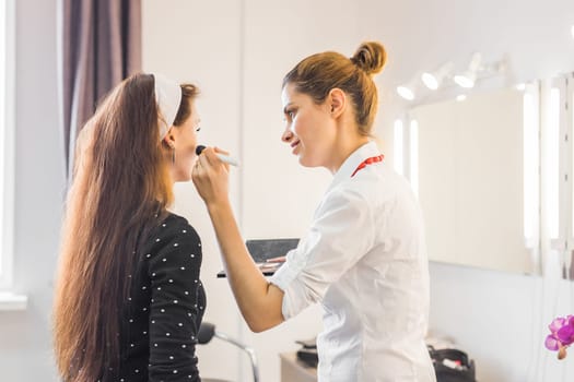 Make-up artist doing make up for young beautiful bride applying wedding make-up