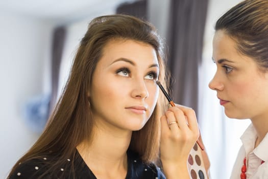 Make-up artist doing make up for young beautiful bride applying wedding make-up