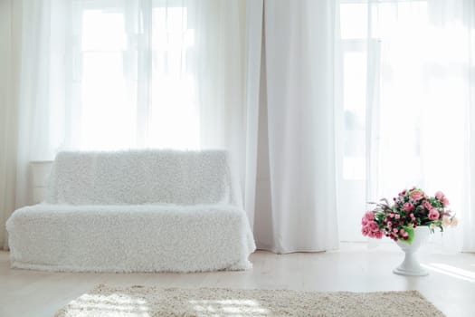 white sofa with flowers in the interior of the white room with windows